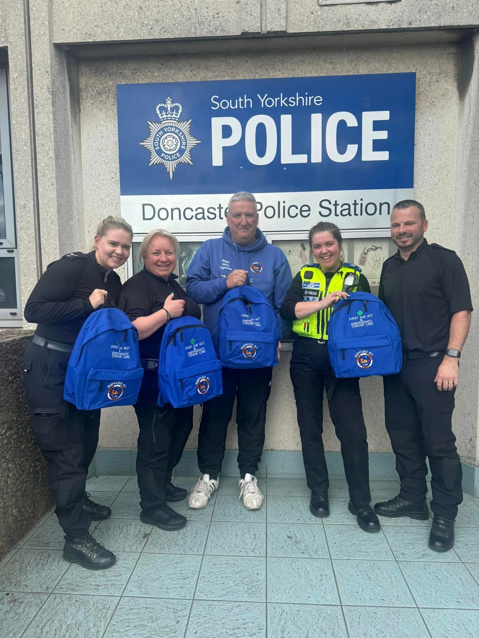 Five people holding blue Sam's Army backpacks outside Doncaster Police Station.